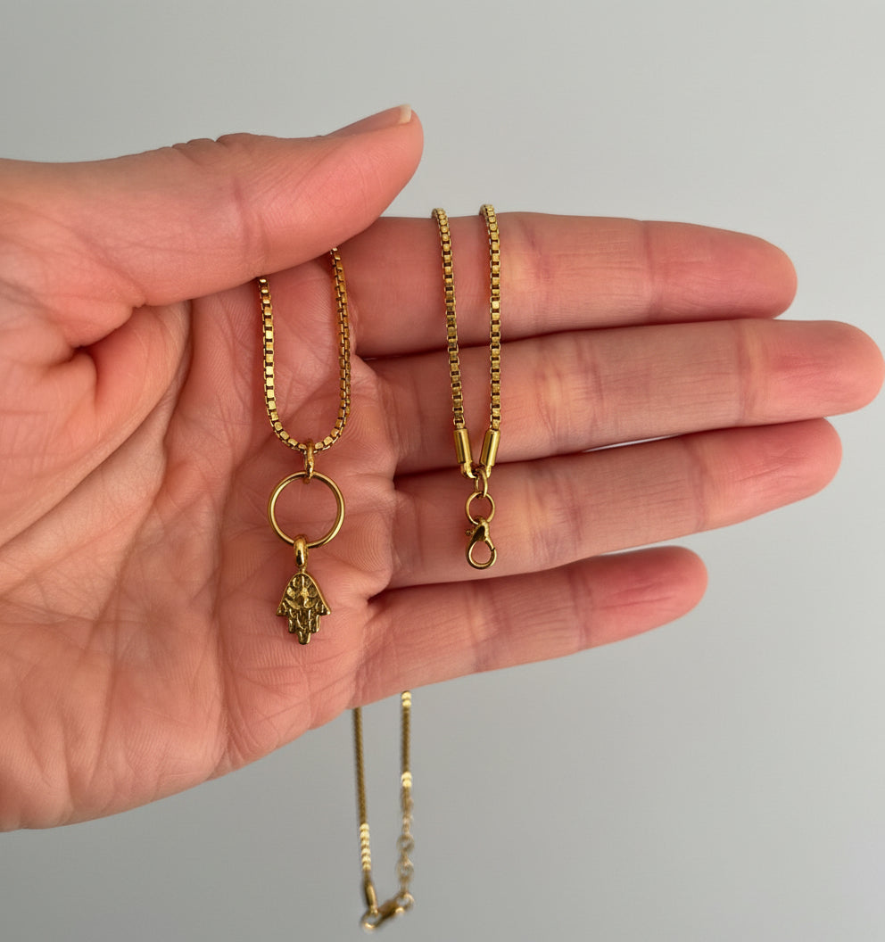 one gold necklaces held in a hand against a neutral background