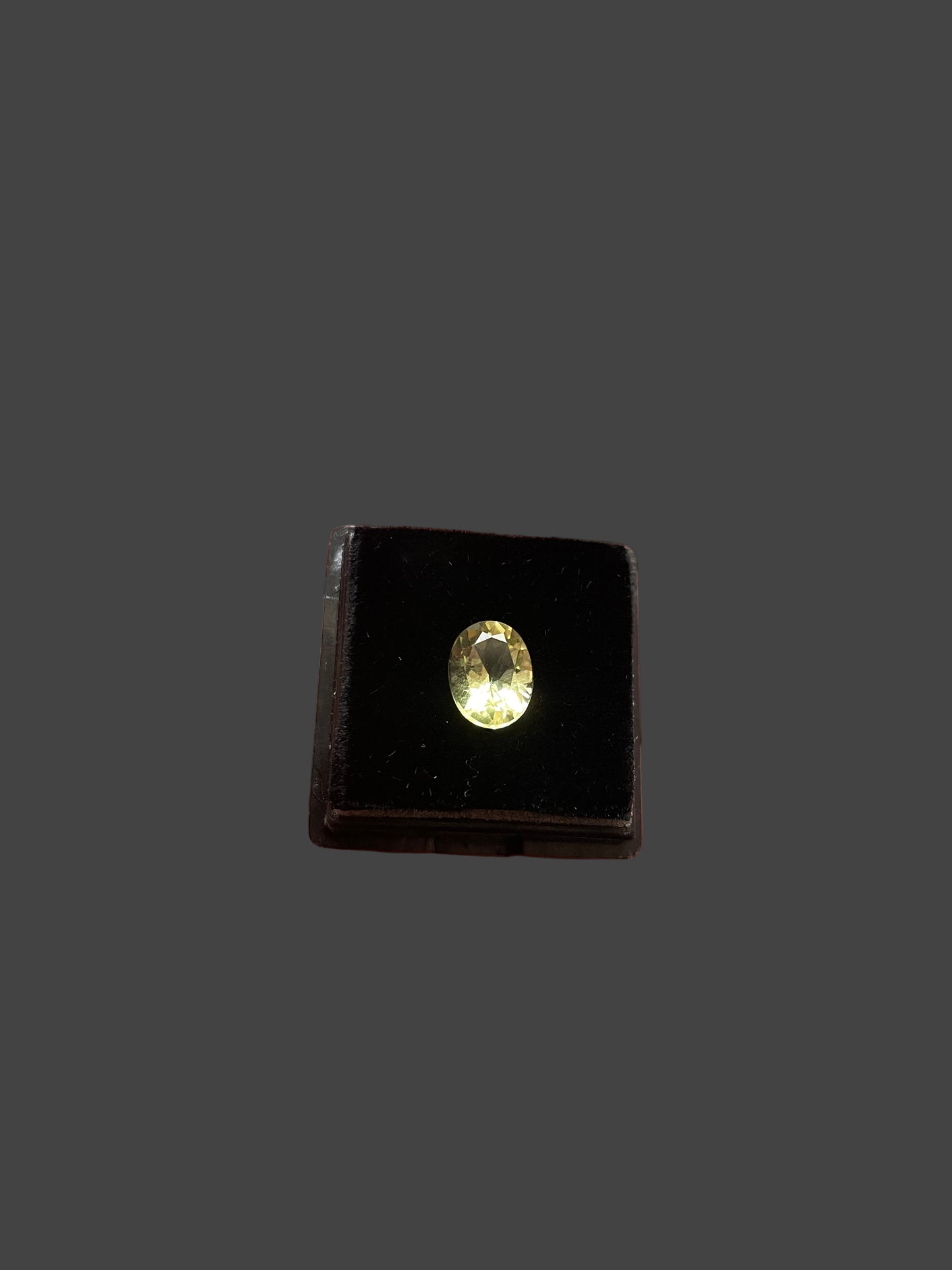 yellow gemstone  in a black box held in a hand with a blurred background