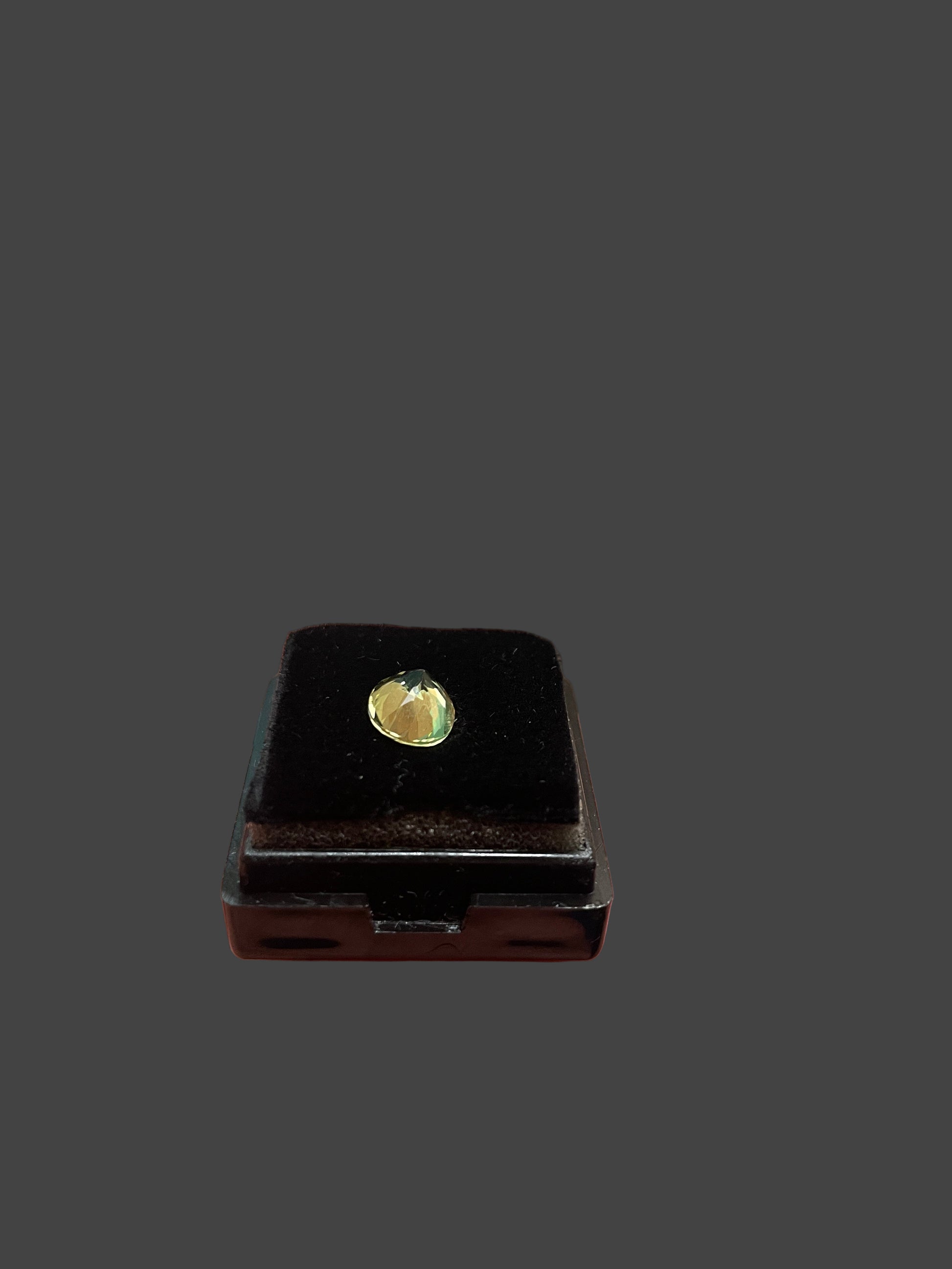 Small black rectangular object with a lemon yellow gemstone held in a hand against a blurred background