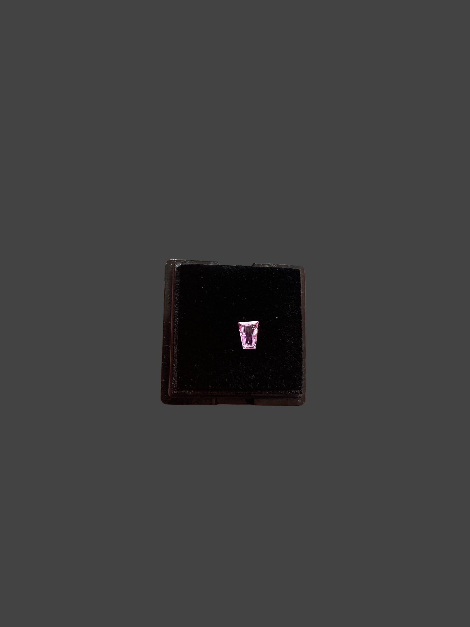 Small black square object with a trapezoid shape gemstone  held in a hand with a blurred backgrounded 