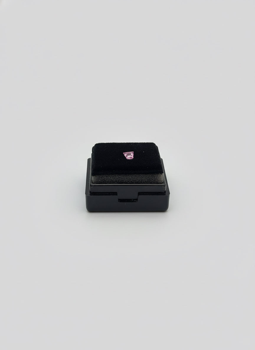 Small black rectangular box with a purplish gemstone trapezoid shape held in a hand with a blurred background