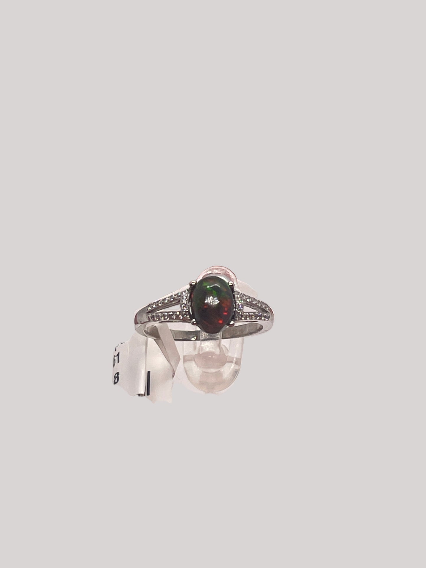 Silver ring with a opal greenish reddish  gemstone held by a hand against a white background