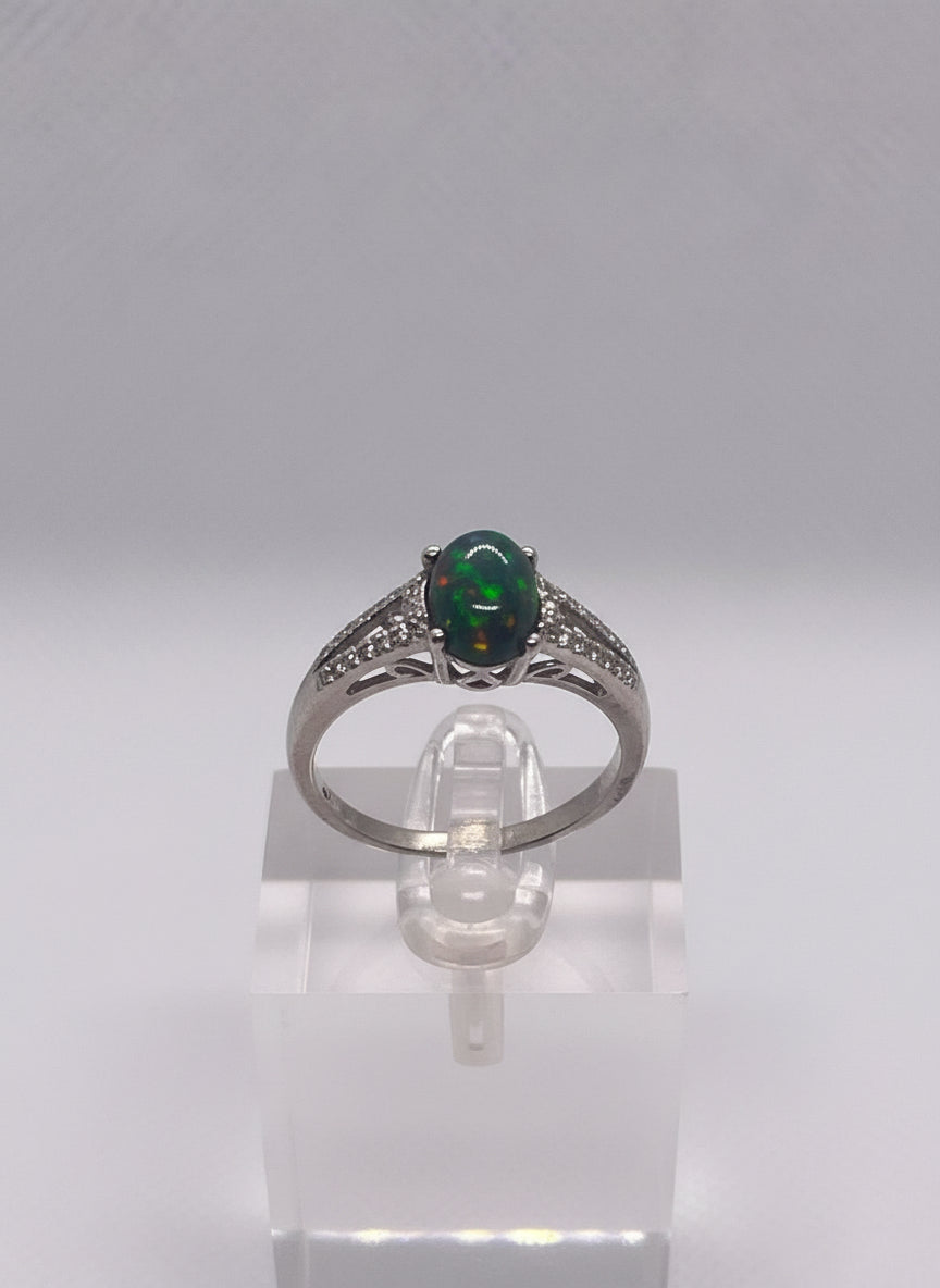 Silver ring with a opal  gemstone on a white stand held by a hand.