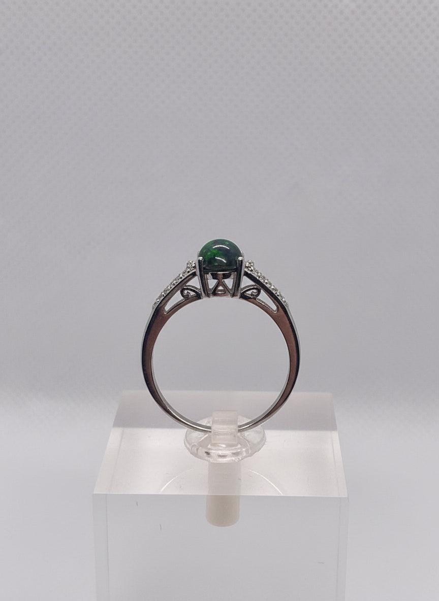 Silver ring with a opal greenish and reddish  gemstone held by a hand against a gray background