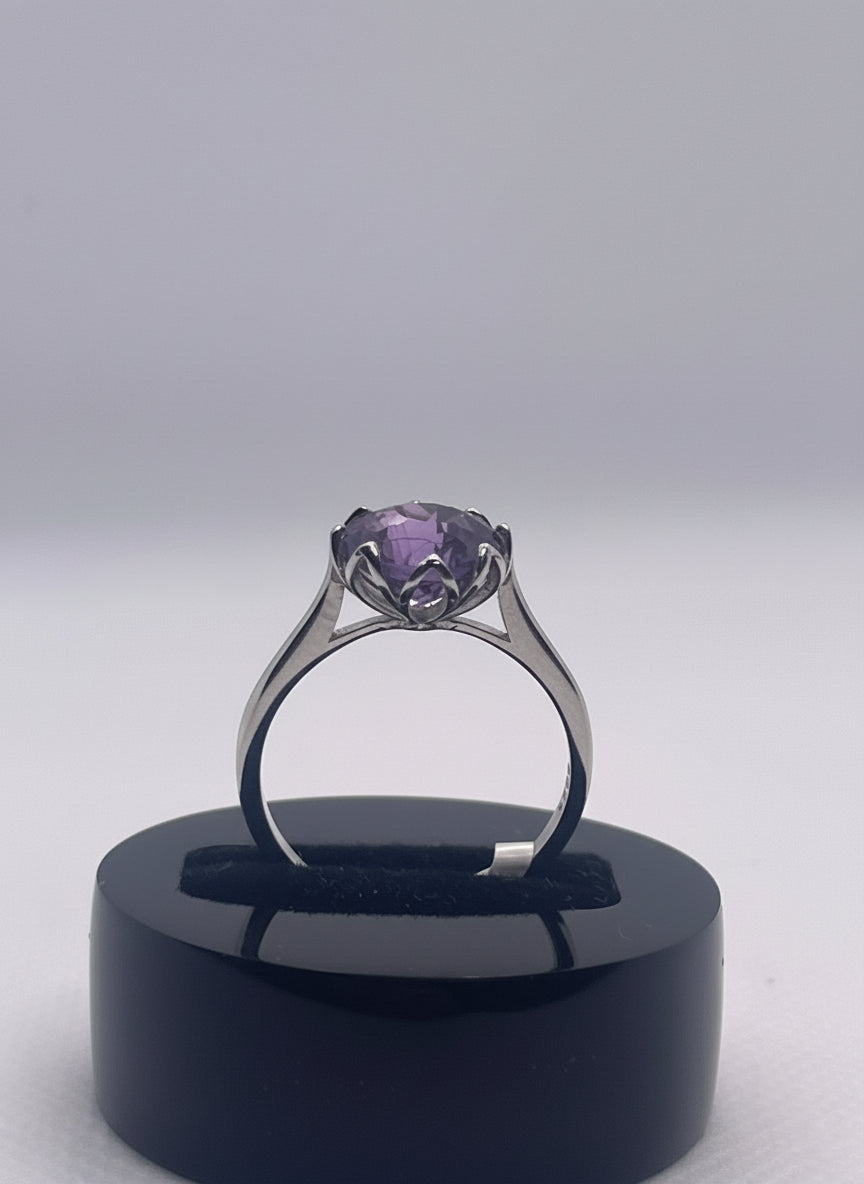 Ring with a purple gemstone on a black stand on a gray background