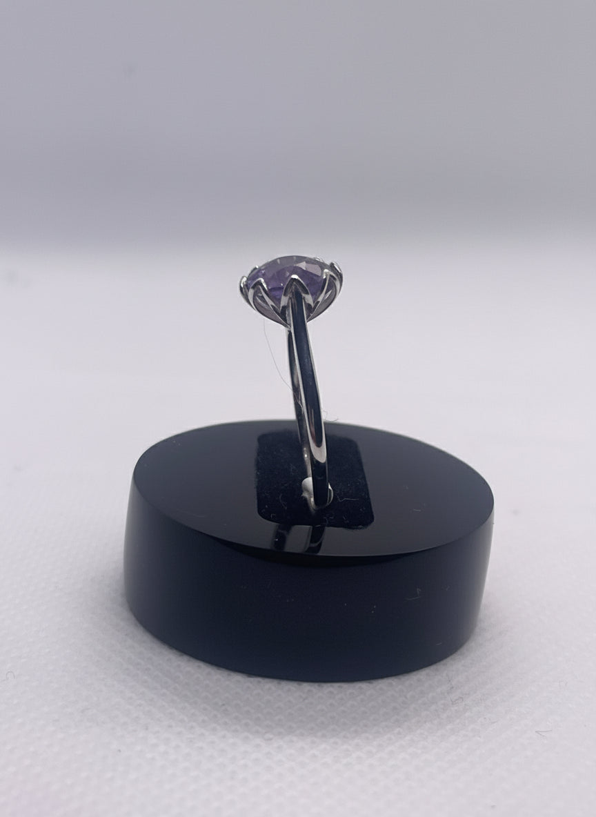 Ring with a purple gemstone on a black stand on a gray background