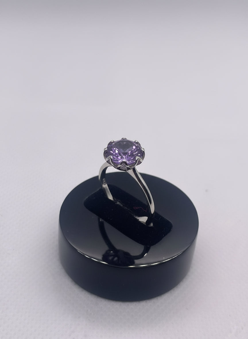 Purple gemstone ring on a black stand against a white background