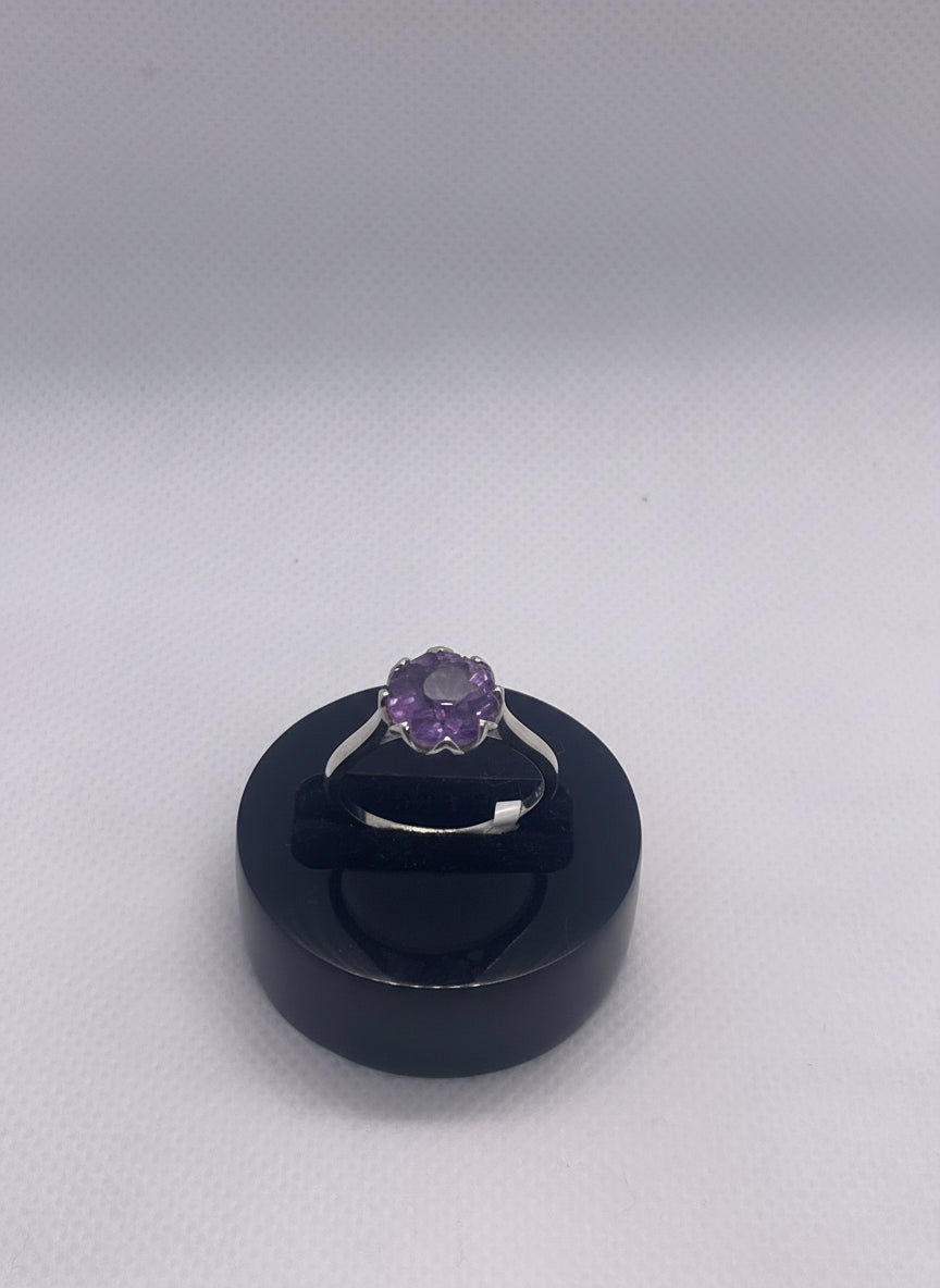 Silver ring with a purple gemstone on a black stand against a light gray background