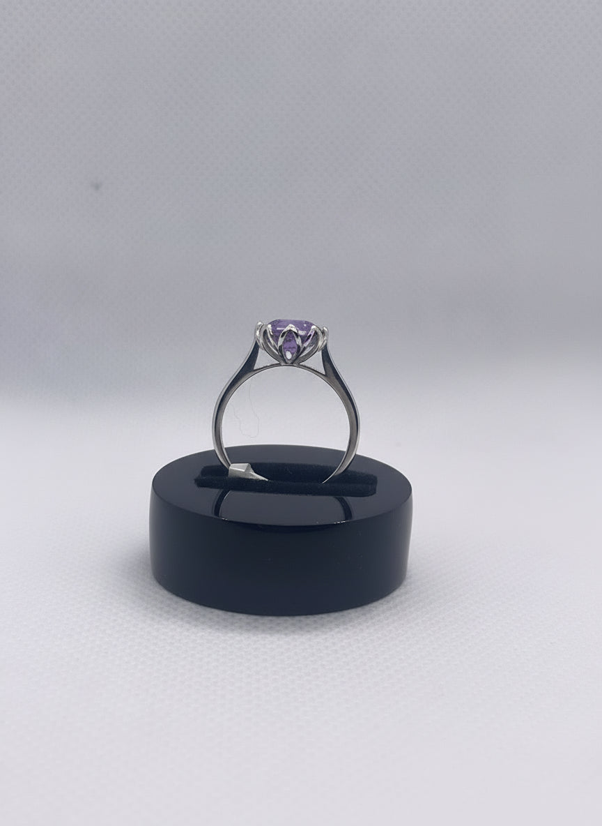 Silver ring with a purple gemstone on a black stand against a light gray background