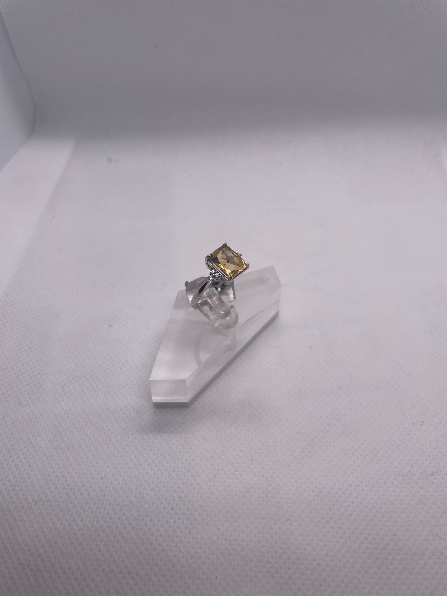 silver ring with a citrino gemstone  on a clear stand against a white background