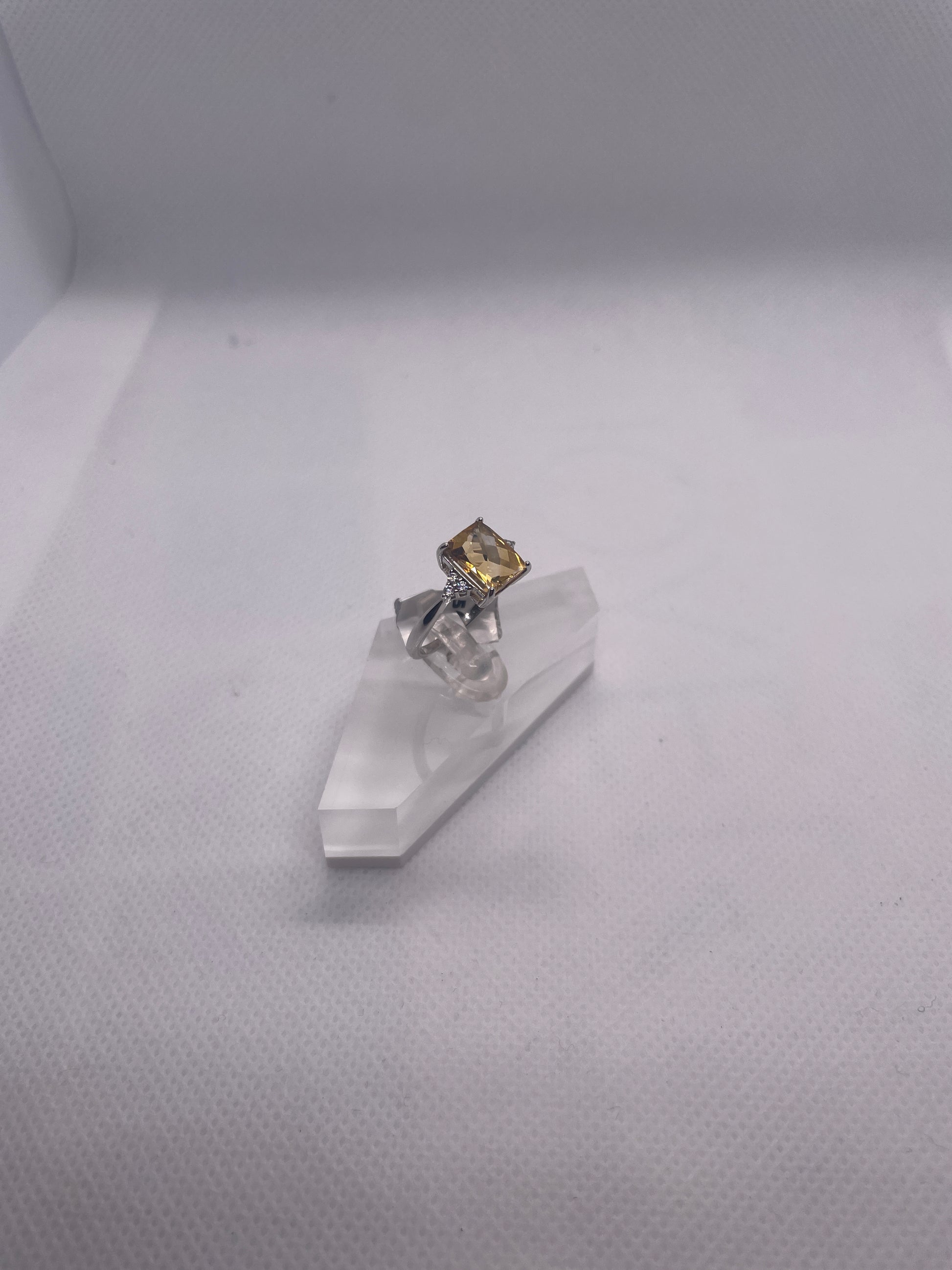 silver ring with a citrino gemstone  on a clear stand against a white background