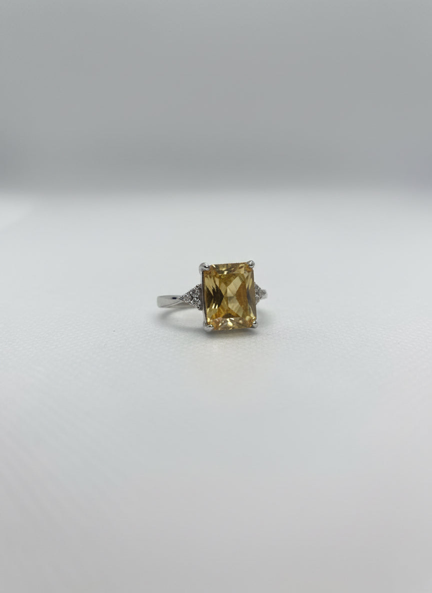 Small ring with a yellow gemstone held in a clear plastic stand on a hand against a white background.