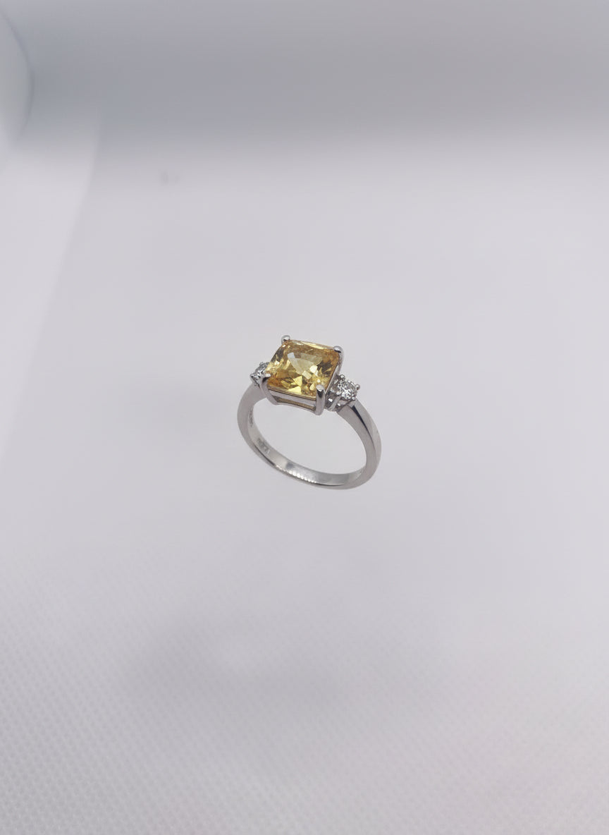 Small ring with a yellow gemstone held in a clear plastic stand on a hand against a white background.