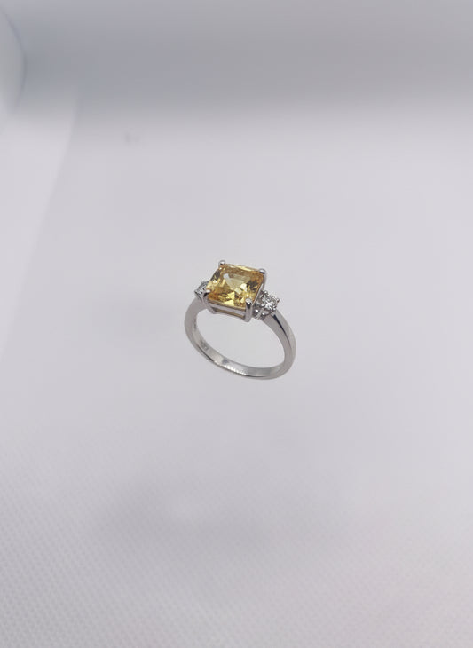 Small ring with a yellow gemstone held in a clear plastic stand on a hand against a white background.