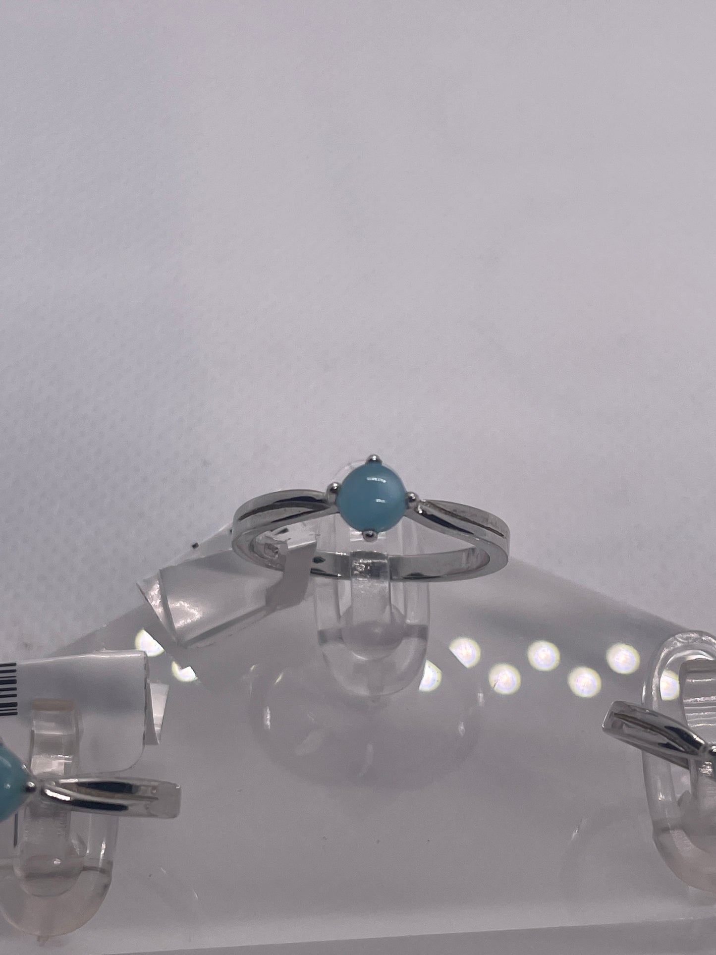 Silver rings with turquoise stones on a clear stand against a white background