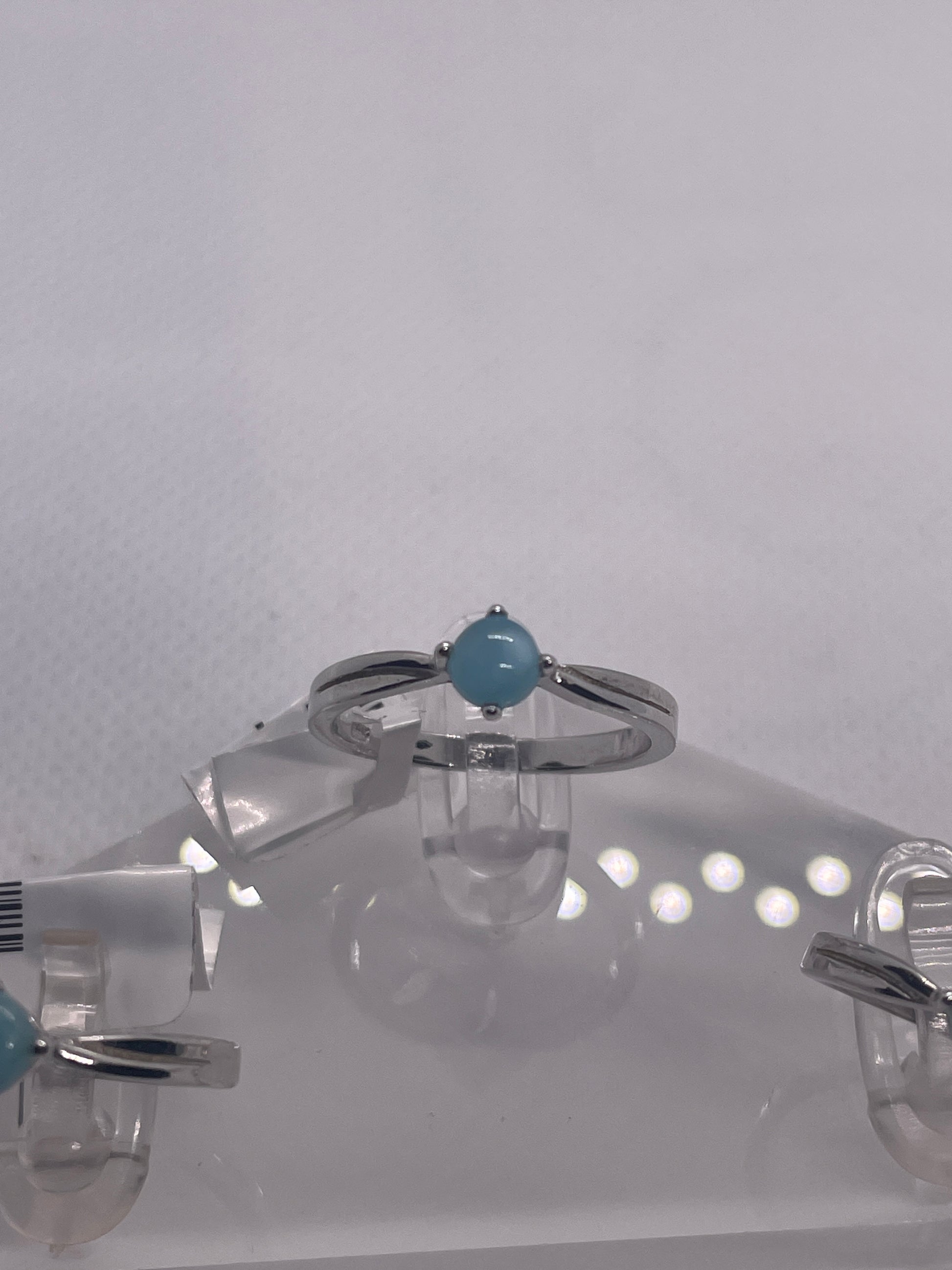 Silver rings with turquoise stones on a clear stand against a white background