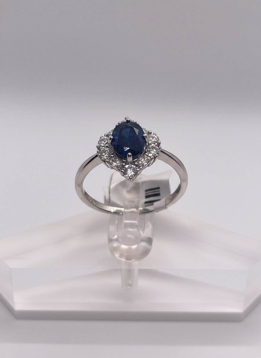 Silver ring with a blue gemstone held by a hand against a white background