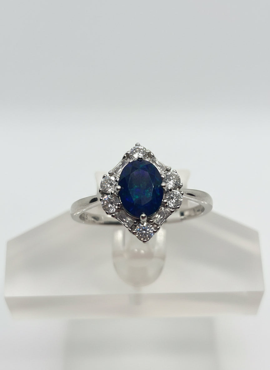 Silver ring with a blue gemstone held by a hand against a white background