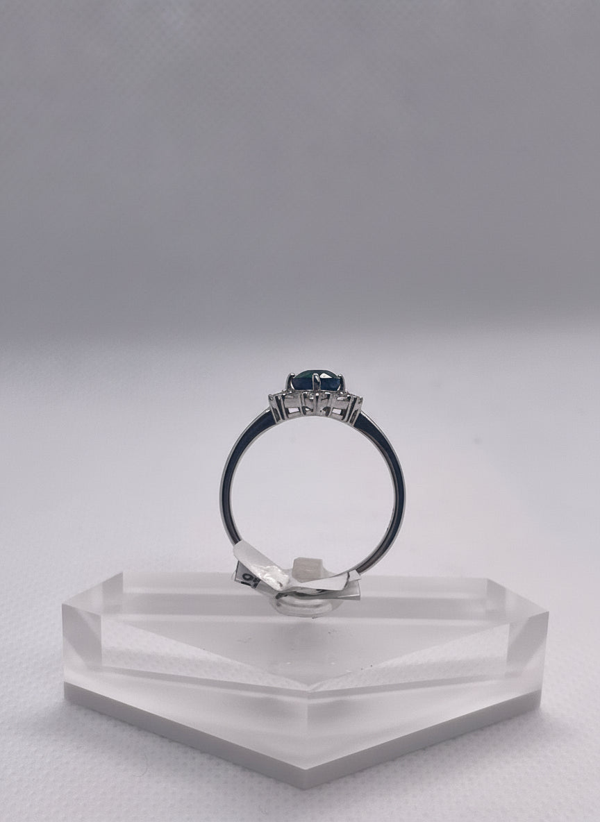 Silver ring with a blue gemstone on a clear stand against a light gray background