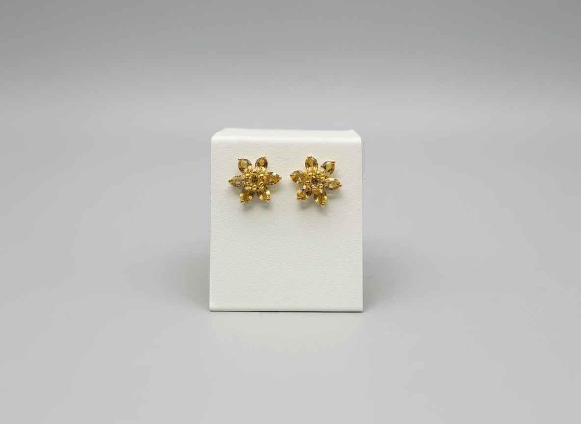 Gold earrings with a golding gemstone floral shaped  on a white card  on a wooden surface and white backg