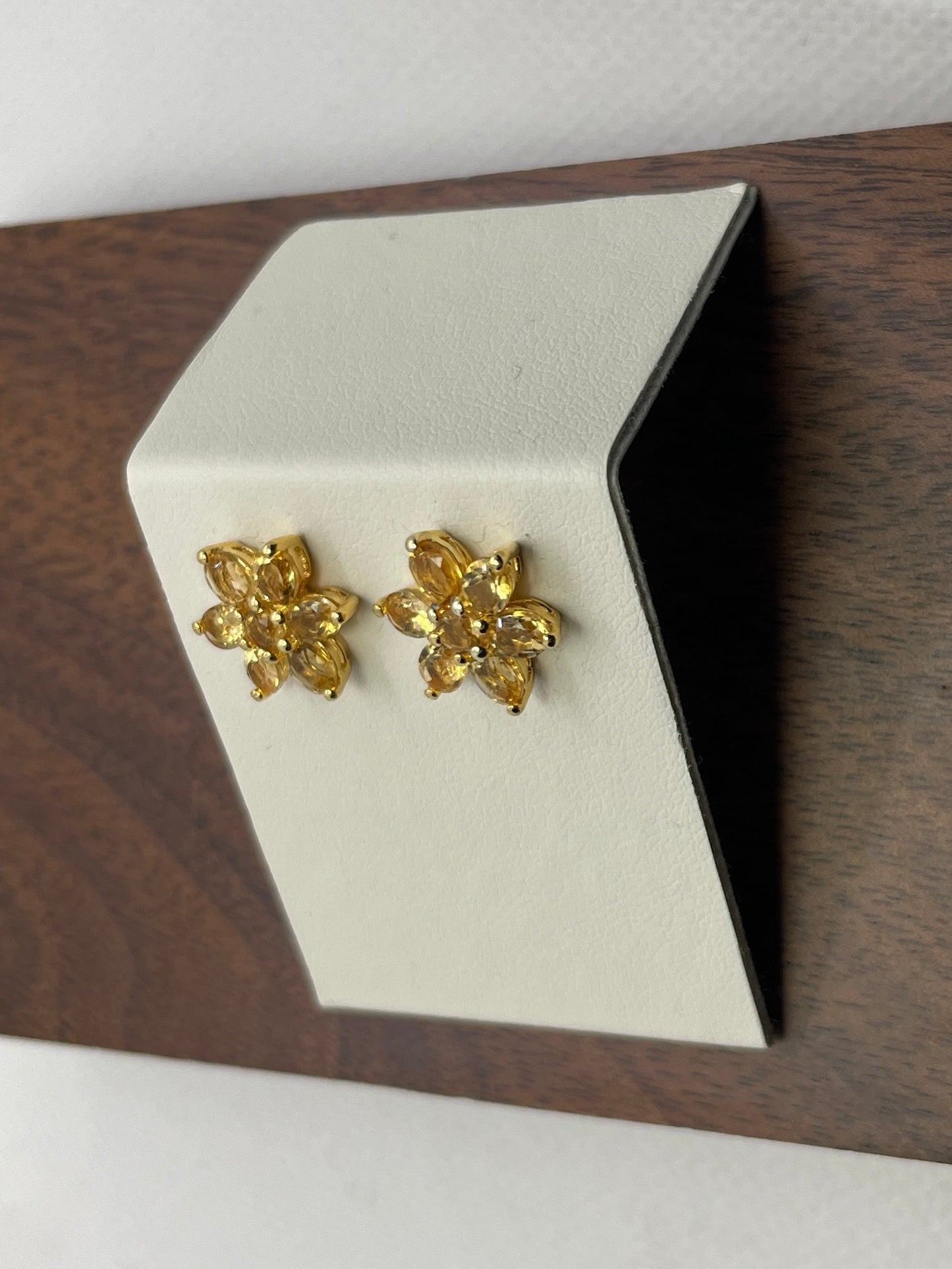 Gold earrings with a golding gemstone floral shaped  on a white card  on a wooden surface and white background